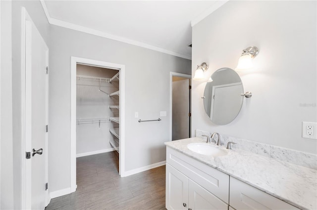 bathroom with vanity, crown molding, wood finished floors, baseboards, and a walk in closet