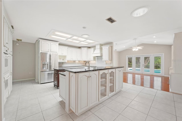 1104 Kells Ct, Lakeland, FL 33813 - kitchen featuring stainless steel refrigerator with ice dispenser, light tile patterned flooring, premium range hood, vaulted ceiling, and glass insert cabinets