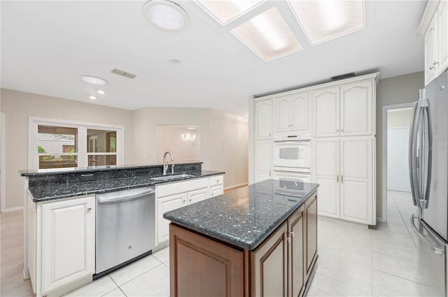 1104 Kells Ct, Lakeland, FL 33813 - kitchen featuring appliances with stainless steel finishes, an island with sink, a sink, white cabinetry, and light tile patterned flooring