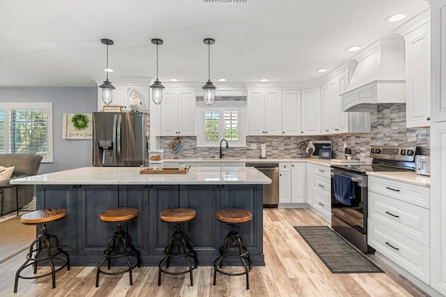 kitchen featuring white cabinets, a kitchen breakfast bar, plenty of natural light, custom range hood, and appliances with stainless steel finishes