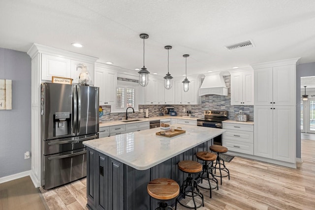 kitchen featuring a sink, visible vents, custom exhaust hood, light wood-style floors, and appliances with stainless steel finishes