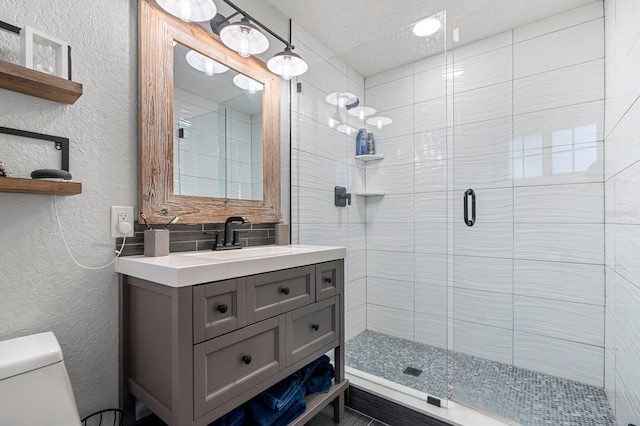 full bath featuring a textured wall, vanity, toilet, and a stall shower