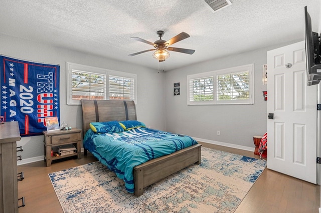 bedroom with a textured ceiling, wood finished floors, visible vents, and baseboards