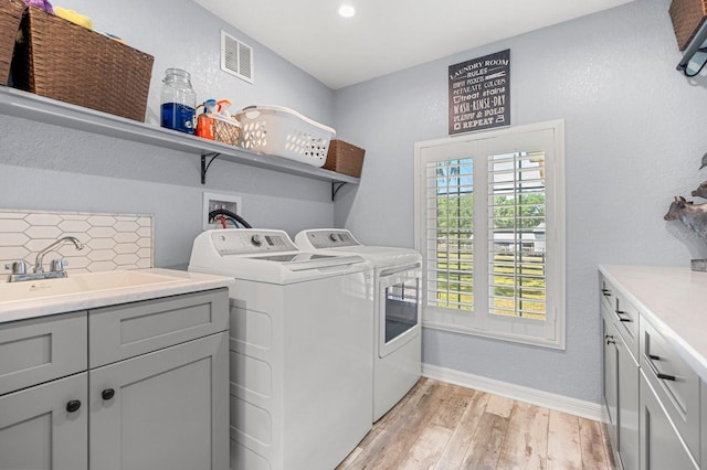 laundry area with visible vents, baseboards, separate washer and dryer, cabinet space, and light wood-style flooring