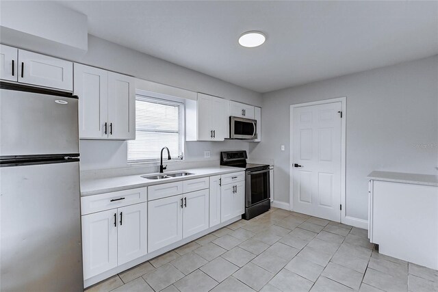 kitchen with a sink, light tile patterned flooring, white cabinetry, light countertops, and appliances with stainless steel finishes