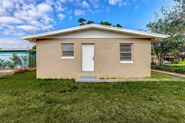 exterior space featuring concrete block siding, a front yard, and fence