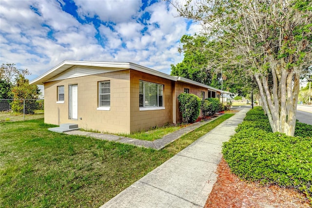 view of property exterior featuring concrete block siding, a lawn, and fence