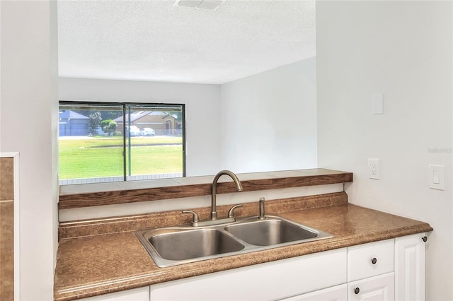 kitchen with white cabinets, dark countertops, a sink, and a textured ceiling