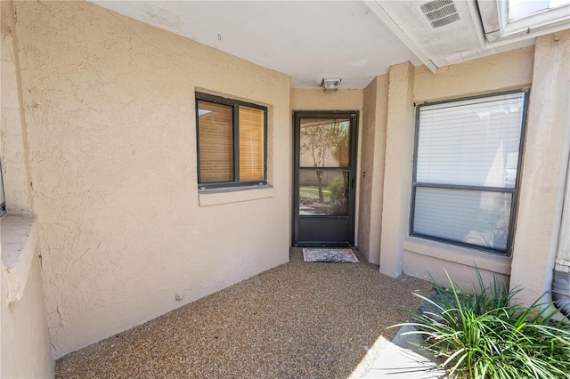 doorway to property featuring stucco siding and visible vents