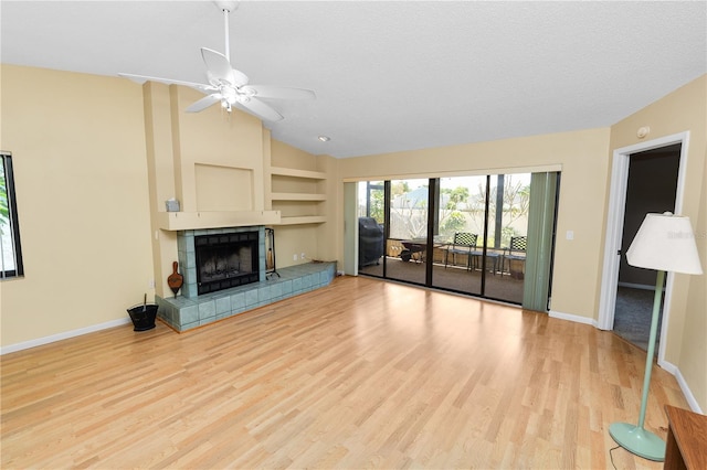 unfurnished living room featuring a tile fireplace, vaulted ceiling, light wood-type flooring, baseboards, and built in shelves