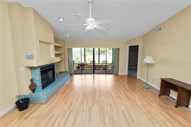 unfurnished living room with baseboards, wood finished floors, visible vents, and a tiled fireplace
