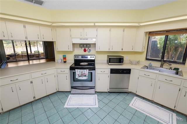kitchen with light countertops, under cabinet range hood, stainless steel appliances, and a sink