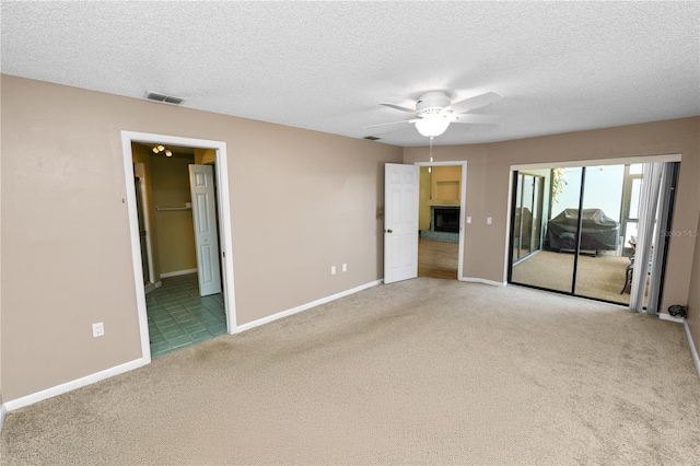 unfurnished bedroom with a textured ceiling, a fireplace with raised hearth, carpet floors, baseboards, and access to exterior