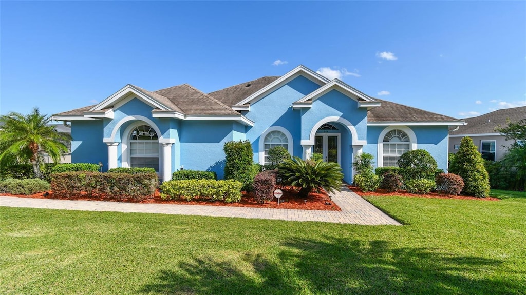 view of front of house featuring roof with shingles, a front lawn, and stucco siding
