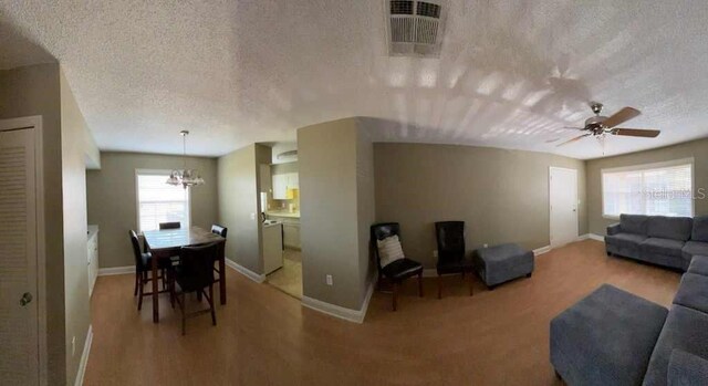 living room featuring a textured ceiling, plenty of natural light, baseboards, and a chandelier