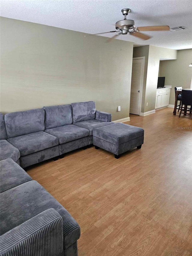 living area featuring a ceiling fan, wood finished floors, baseboards, and a textured ceiling