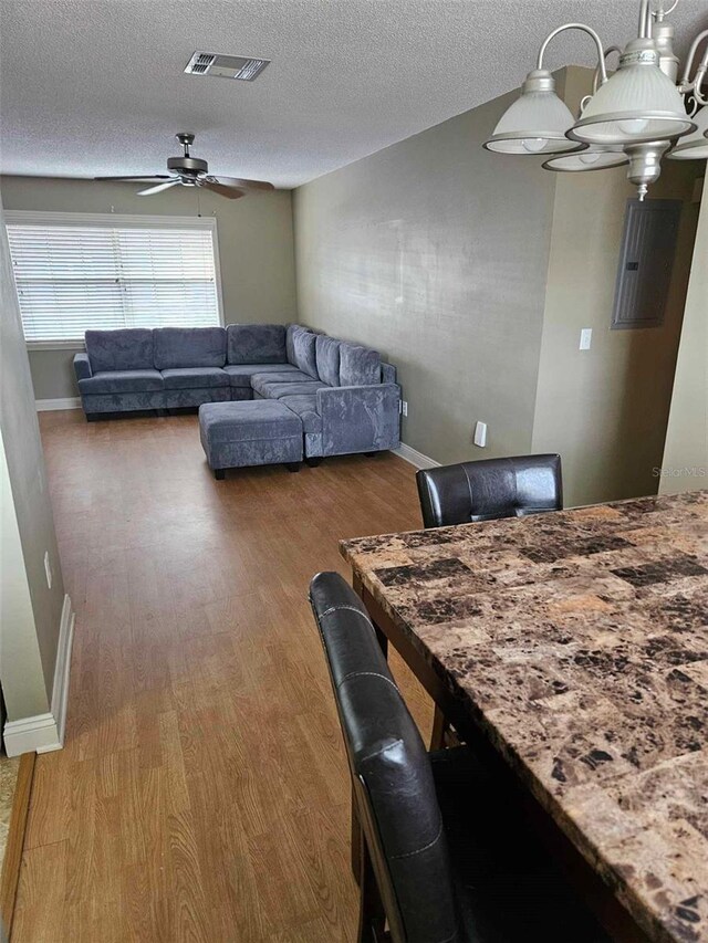 dining room with a ceiling fan, electric panel, wood finished floors, a textured ceiling, and baseboards