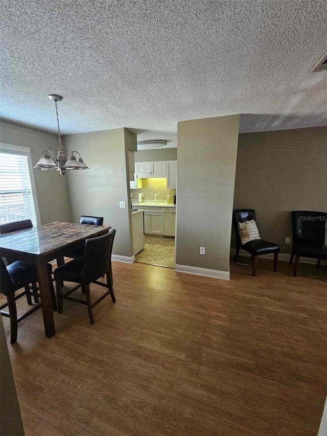 dining space with a chandelier, wood finished floors, a textured ceiling, and baseboards