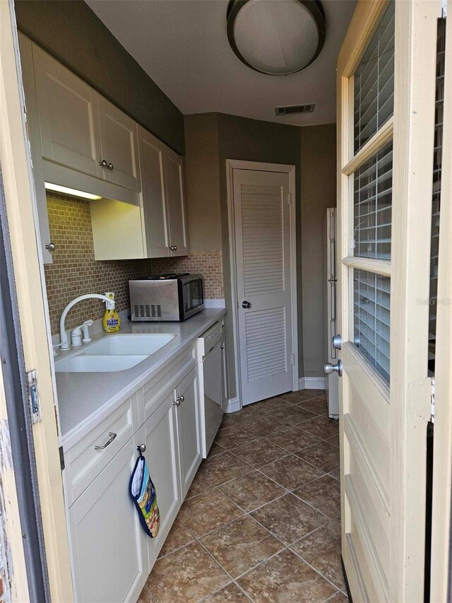 kitchen with a sink, stainless steel microwave, white dishwasher, tasteful backsplash, and light countertops