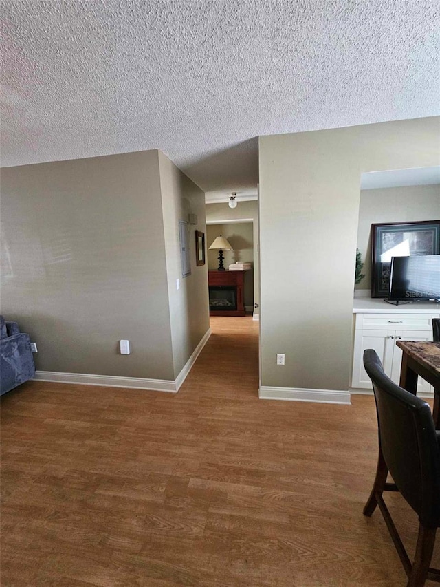 corridor with a textured ceiling, wood finished floors, and baseboards