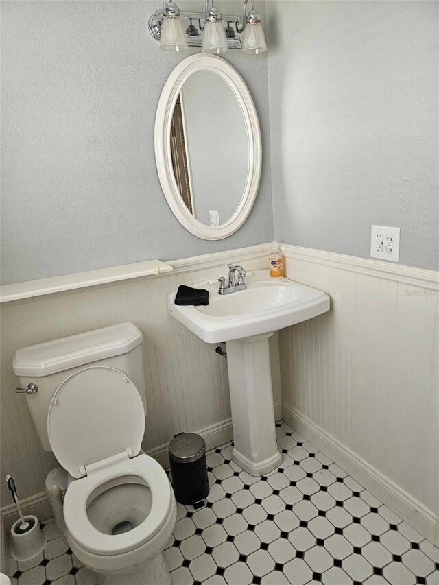 half bathroom featuring wainscoting, tile patterned floors, and toilet