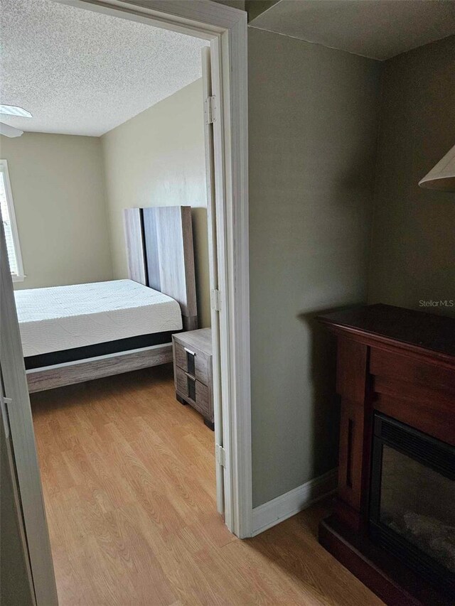 bedroom featuring light wood finished floors, a glass covered fireplace, baseboards, and a textured ceiling