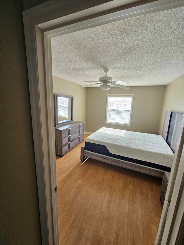bedroom with multiple windows, light wood-style flooring, a ceiling fan, and a textured ceiling