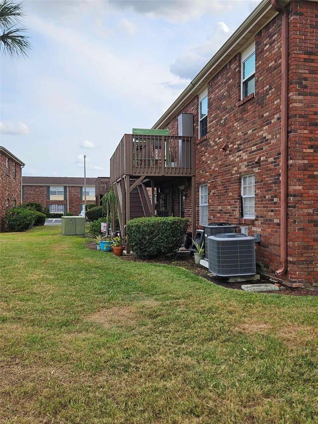 view of grassy yard with a deck, central air condition unit, and stairway