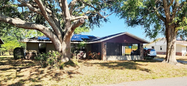 view of front facade featuring solar panels, a sunroom, stone siding, and a front lawn