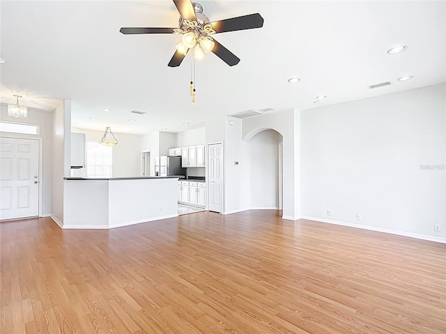 unfurnished living room with visible vents, arched walkways, light wood finished floors, and baseboards