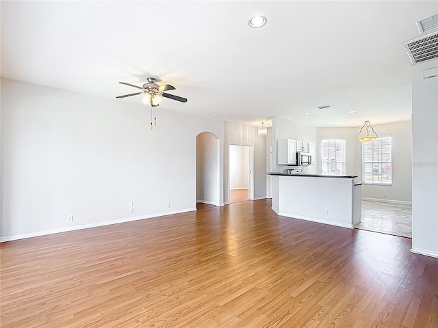 unfurnished living room featuring visible vents, a ceiling fan, light wood-style floors, baseboards, and arched walkways
