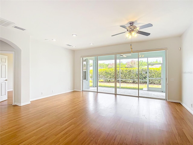 spare room with ceiling fan, visible vents, arched walkways, light wood-type flooring, and baseboards