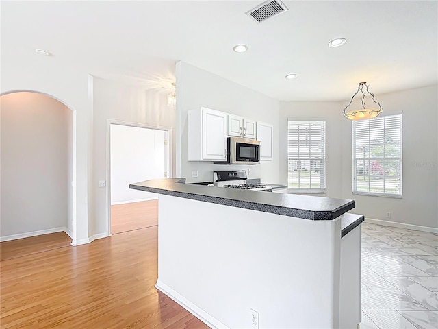 kitchen featuring dark countertops, arched walkways, stainless steel microwave, gas range, and visible vents