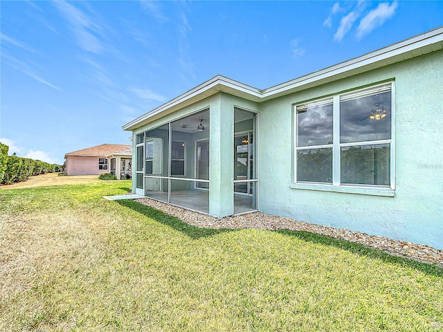 rear view of property with a lawn, a sunroom, and stucco siding