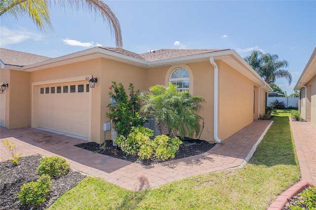 view of home's exterior featuring stucco siding, fence, decorative driveway, and a garage
