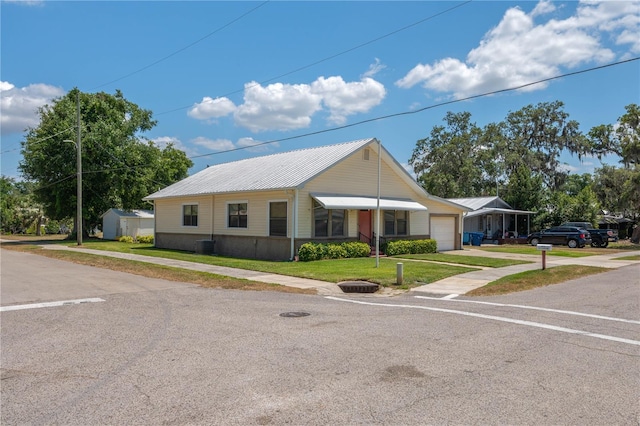 view of front facade featuring metal roof, a front yard, a garage, an outdoor structure, and a storage unit
