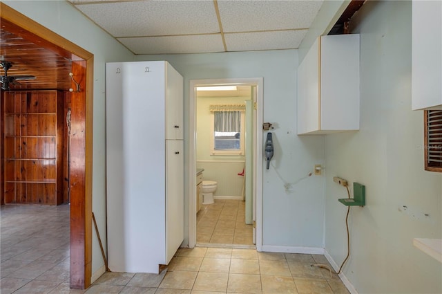 hallway featuring light tile patterned floors, baseboards, and a paneled ceiling