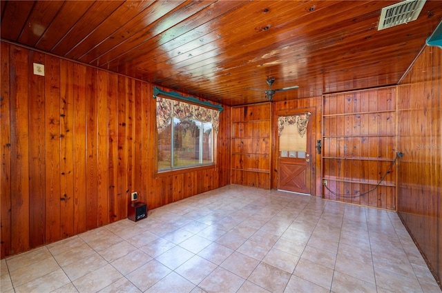 empty room featuring wooden walls, light tile patterned floors, visible vents, and wood ceiling