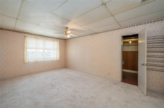 unfurnished bedroom featuring carpet flooring, ceiling fan, wallpapered walls, baseboards, and a drop ceiling