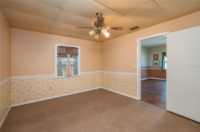 carpeted spare room with a healthy amount of sunlight, a ceiling fan, a paneled ceiling, and visible vents