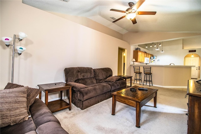 living area featuring ceiling fan, visible vents, baseboards, vaulted ceiling, and light carpet