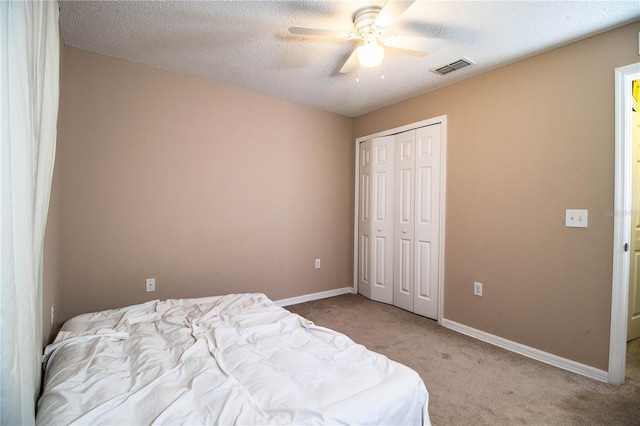 carpeted bedroom featuring a closet, ceiling fan, visible vents, baseboards, and a textured ceiling