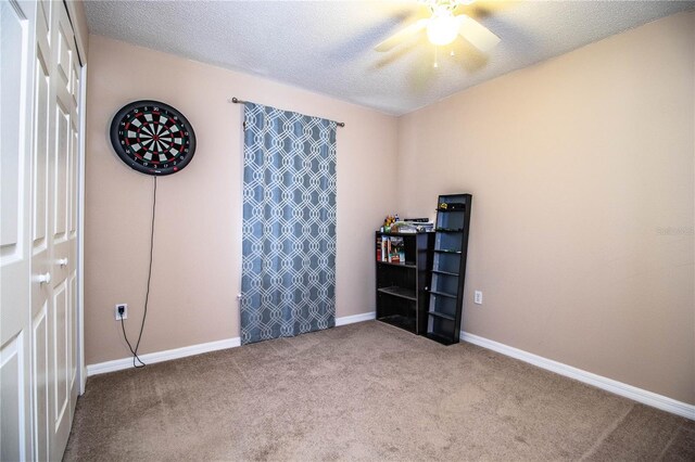 carpeted spare room with a textured ceiling, a ceiling fan, and baseboards