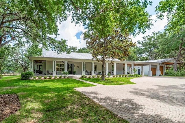 ranch-style house featuring covered porch, a chimney, metal roof, a front yard, and decorative driveway
