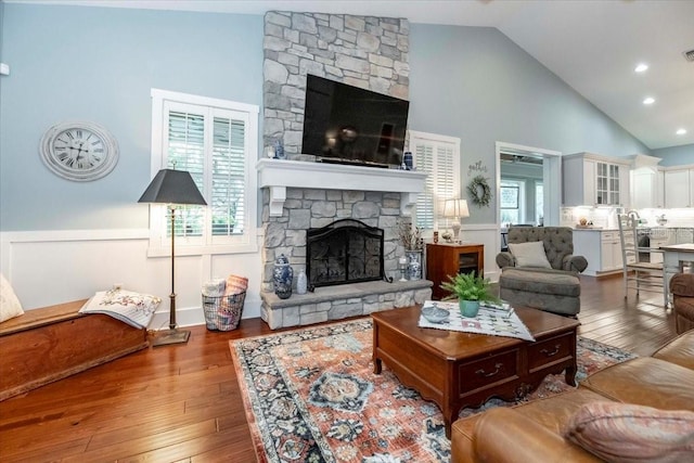 living area with wainscoting, a fireplace, high vaulted ceiling, hardwood / wood-style floors, and visible vents