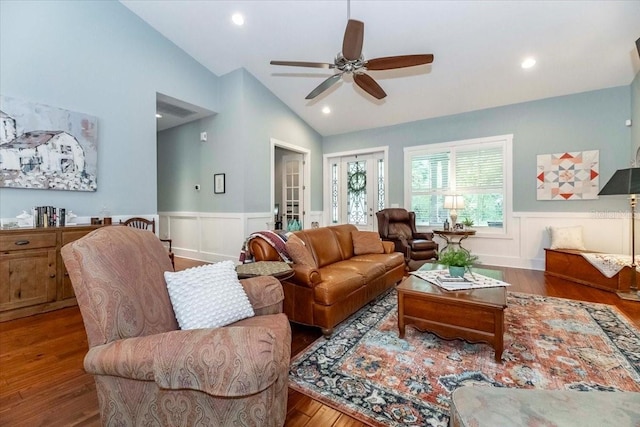 living room featuring wainscoting, a decorative wall, a ceiling fan, wood finished floors, and lofted ceiling