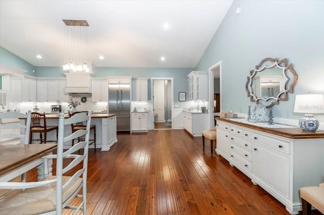 kitchen with decorative backsplash, a breakfast bar area, stainless steel built in fridge, white cabinets, and dark wood finished floors