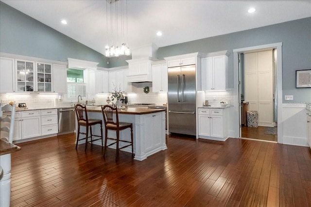kitchen featuring decorative backsplash, a kitchen island, white cabinets, custom range hood, and appliances with stainless steel finishes