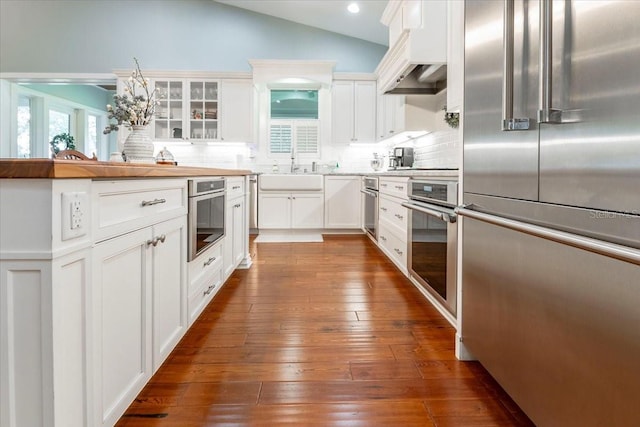 kitchen with vaulted ceiling, a sink, white cabinets, glass insert cabinets, and stainless steel appliances