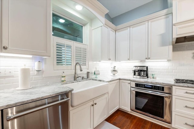 kitchen with decorative backsplash, appliances with stainless steel finishes, light stone countertops, a sink, and white cabinetry